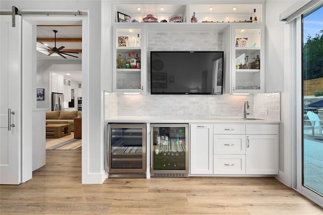 bar with light wood-type flooring, wine cooler, a sink, and tasteful backsplash