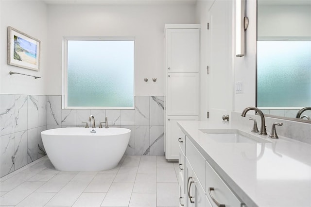 full bathroom with wainscoting, tile patterned floors, vanity, a freestanding tub, and tile walls