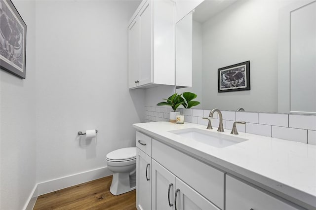 bathroom with baseboards, toilet, wood finished floors, vanity, and backsplash