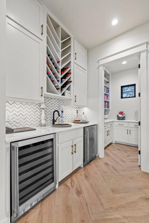 bar with tasteful backsplash, wine cooler, stainless steel refrigerator, wet bar, and a sink