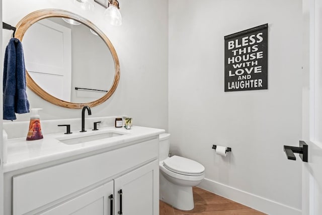 half bath with toilet, baseboards, wood finished floors, and vanity