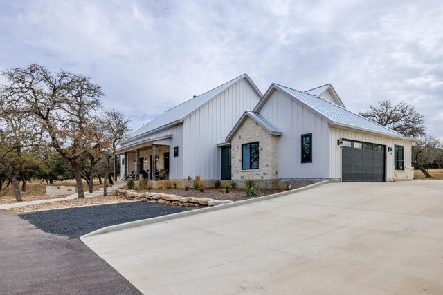 view of front of home with concrete driveway, stone siding, metal roof, an attached garage, and board and batten siding