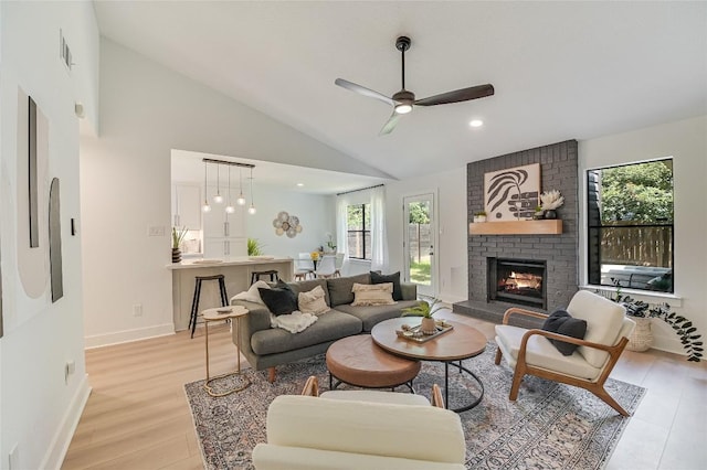 living room featuring a fireplace, light wood-style flooring, a ceiling fan, high vaulted ceiling, and baseboards