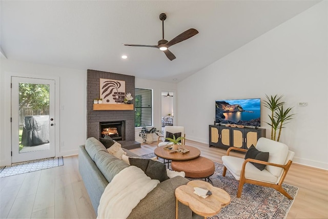 living area with light wood-style floors, vaulted ceiling, a fireplace, and ceiling fan