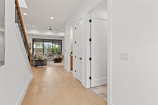 corridor featuring baseboards, stairs, light wood-style flooring, and recessed lighting