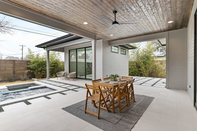 view of patio / terrace featuring an in ground hot tub, fence, a ceiling fan, and outdoor dining space