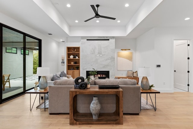 living room with ceiling fan, a tile fireplace, recessed lighting, baseboards, and light wood-style floors