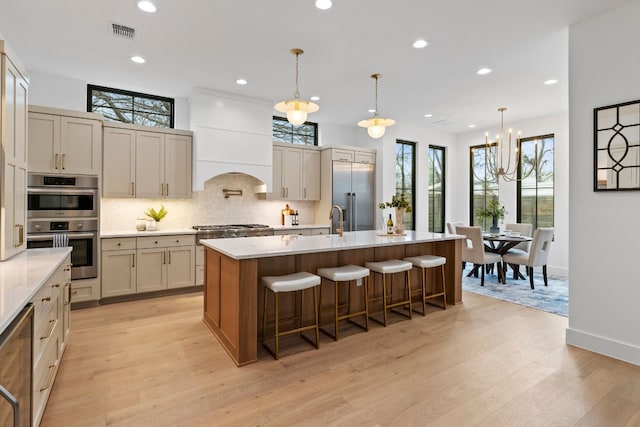 kitchen featuring visible vents, an island with sink, stainless steel appliances, premium range hood, and pendant lighting