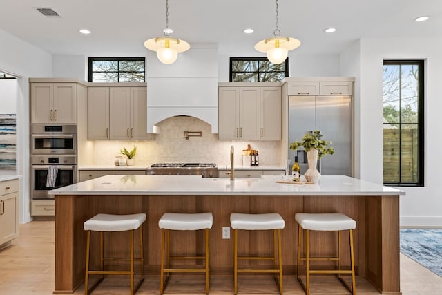 kitchen featuring a breakfast bar, stainless steel appliances, light countertops, visible vents, and a kitchen island with sink