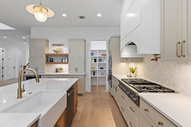 kitchen with light stone counters, open shelves, stainless steel appliances, hanging light fixtures, and a sink