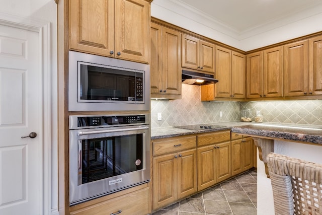 kitchen with brown cabinets, tasteful backsplash, appliances with stainless steel finishes, ornamental molding, and under cabinet range hood