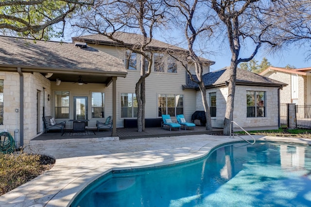 rear view of property featuring a shingled roof, fence, a ceiling fan, stone siding, and a fenced in pool