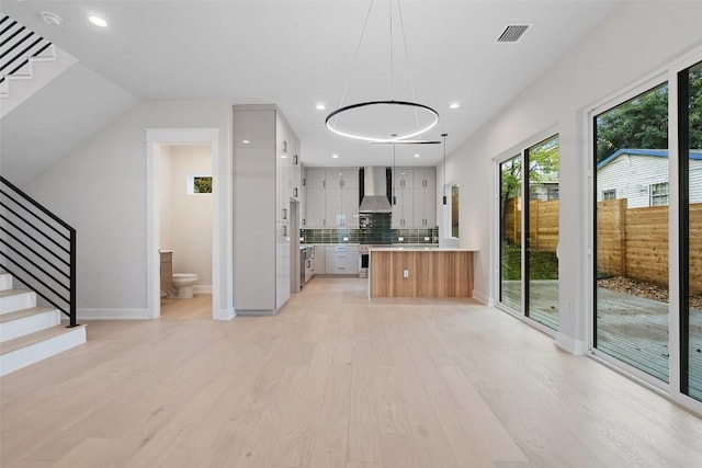 1135 Salina St, Austin, TX 78702 - kitchen with wall chimney exhaust hood, light countertops, light wood-style flooring, backsplash, and modern cabinets
