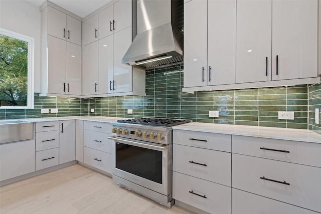 1135 Salina St, Austin, TX 78702 - kitchen with stainless steel stove, wall chimney range hood, decorative backsplash, and light stone counters