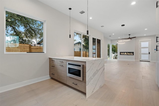 1135 Salina St, Austin, TX 78702 - kitchen featuring light wood-type flooring, stainless steel microwave, modern cabinets, recessed lighting, and a glass covered fireplace