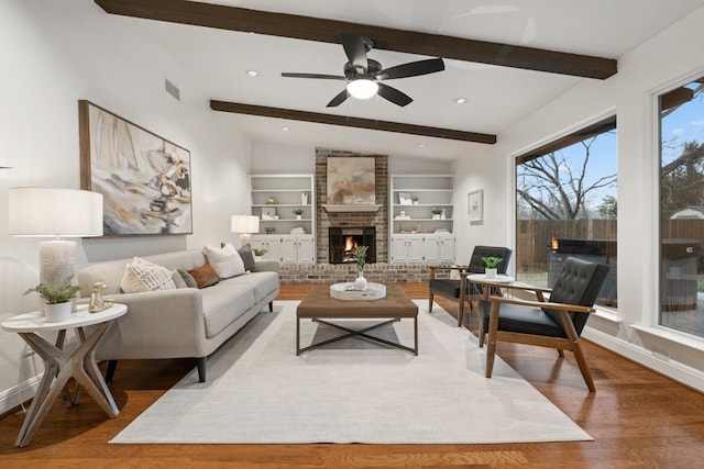 living room featuring visible vents, wood finished floors, vaulted ceiling with beams, built in shelves, and a fireplace