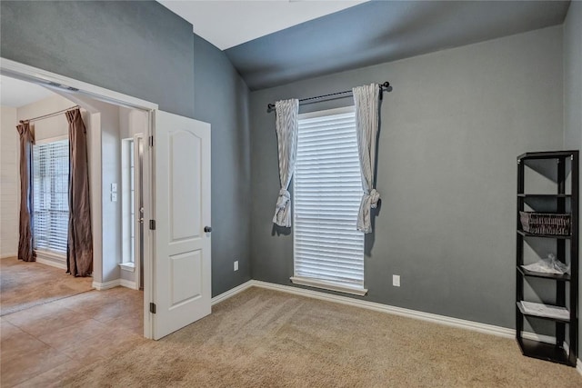 empty room featuring baseboards, arched walkways, lofted ceiling, and light colored carpet