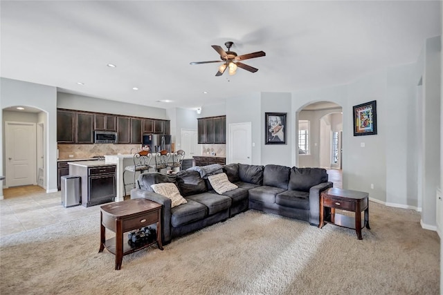 living area with arched walkways, light colored carpet, a ceiling fan, light tile patterned flooring, and baseboards