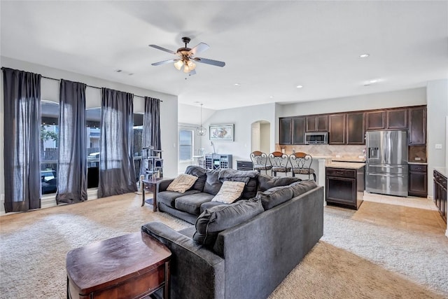 living area with arched walkways, lofted ceiling, visible vents, light carpet, and ceiling fan