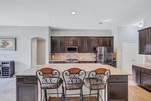 kitchen featuring appliances with stainless steel finishes, a kitchen island, dark brown cabinets, and light stone countertops