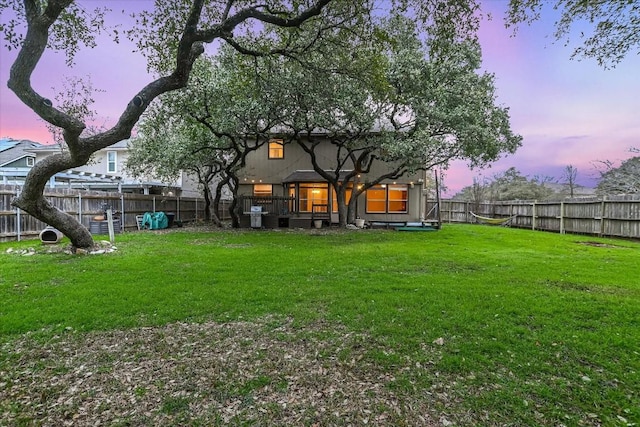 back of house at dusk featuring a fenced backyard and a yard