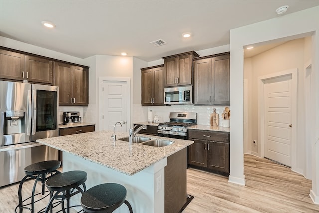 kitchen with stainless steel appliances, visible vents, light wood-style floors, a kitchen island with sink, and light stone countertops