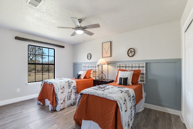 bedroom featuring baseboards, a textured ceiling, visible vents, and wood finished floors