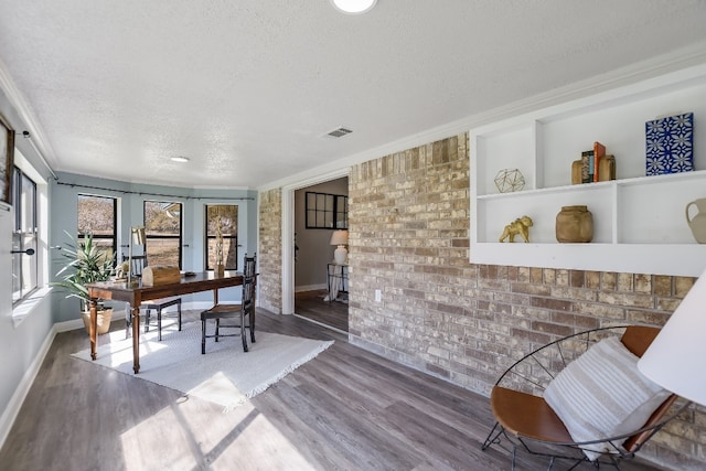 office area featuring a textured ceiling, brick wall, wood finished floors, visible vents, and ornamental molding