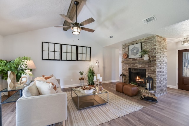 living room featuring visible vents, lofted ceiling, wood finished floors, a textured ceiling, and a brick fireplace