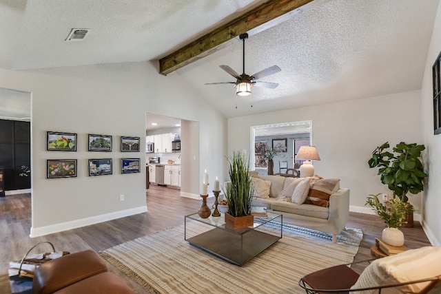 living area featuring baseboards, visible vents, wood finished floors, vaulted ceiling with beams, and a textured ceiling