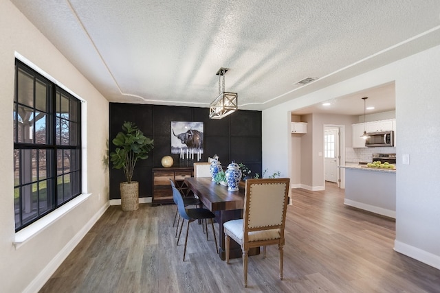 dining space featuring a textured ceiling, wood finished floors, visible vents, and baseboards