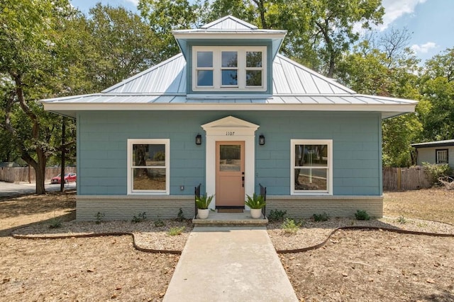 bungalow-style home with a standing seam roof, fence, metal roof, and brick siding