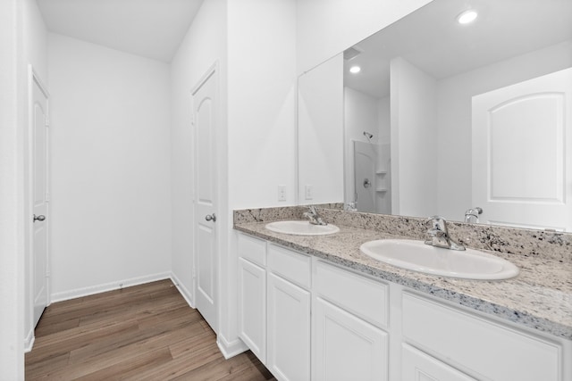 bathroom featuring double vanity, wood finished floors, a shower, and a sink