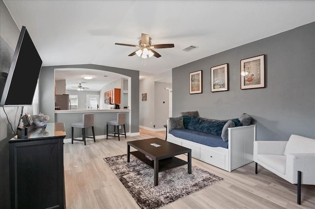 living room featuring arched walkways, visible vents, light wood-style flooring, ceiling fan, and baseboards