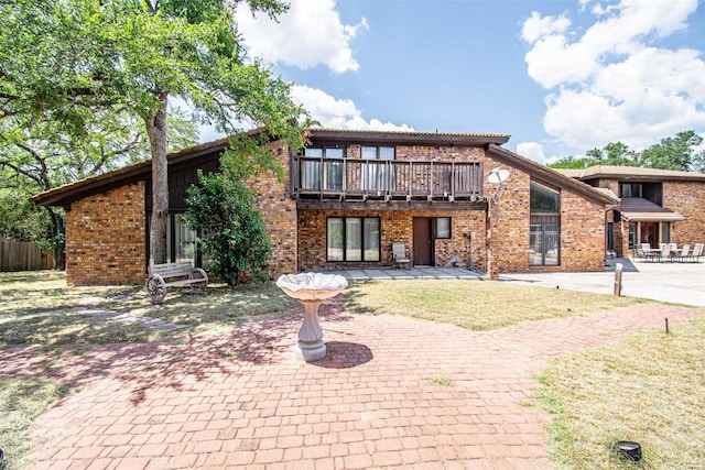 rear view of house with a patio, brick siding, and a balcony