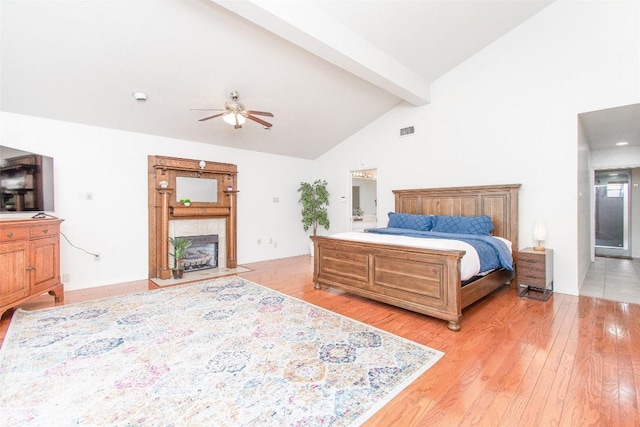 bedroom featuring high vaulted ceiling, a fireplace, visible vents, light wood-style floors, and beam ceiling