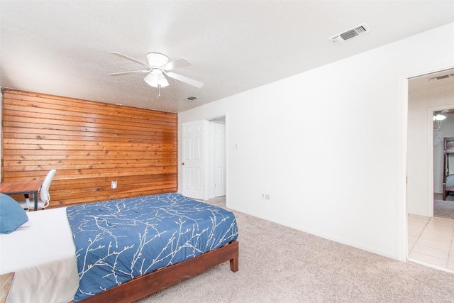 bedroom with light carpet, wood walls, visible vents, and a ceiling fan