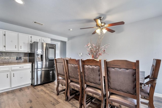 kitchen featuring light wood finished floors, stainless steel fridge, visible vents, white cabinets, and backsplash