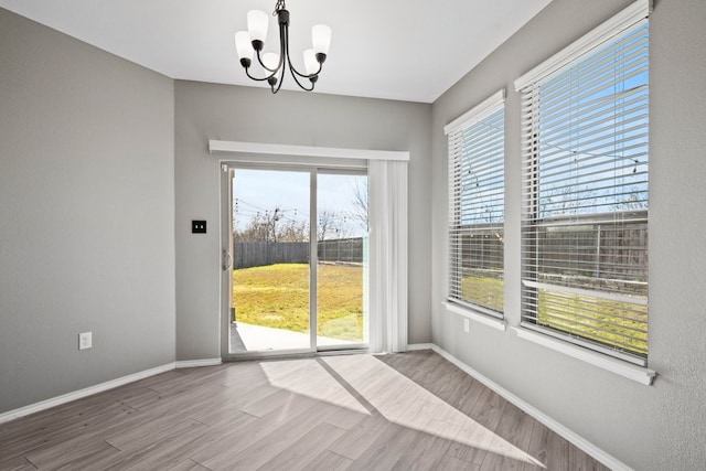 unfurnished dining area with plenty of natural light, baseboards, a chandelier, and wood finished floors