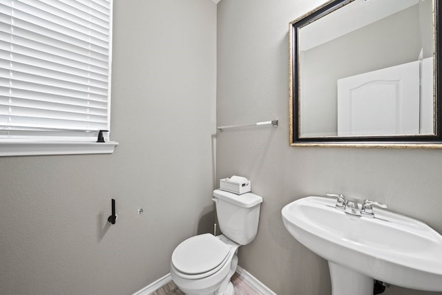 half bathroom featuring wood finished floors, a sink, toilet, and baseboards