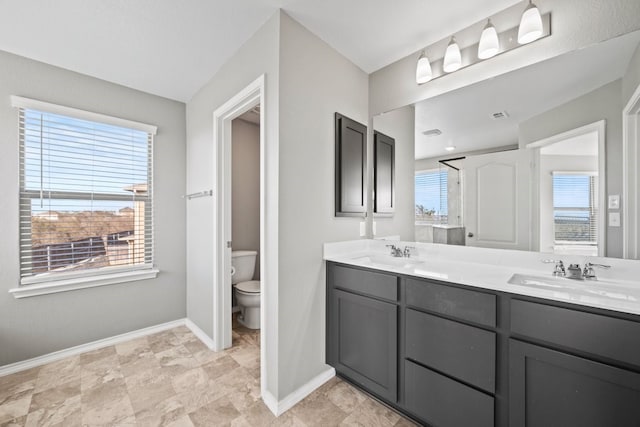 bathroom featuring toilet, double vanity, baseboards, and a sink