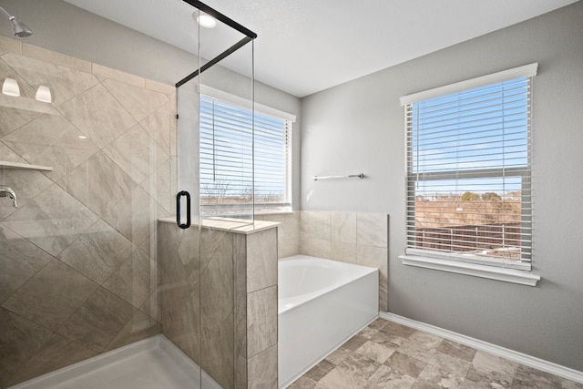 bathroom with a stall shower, a bath, and baseboards