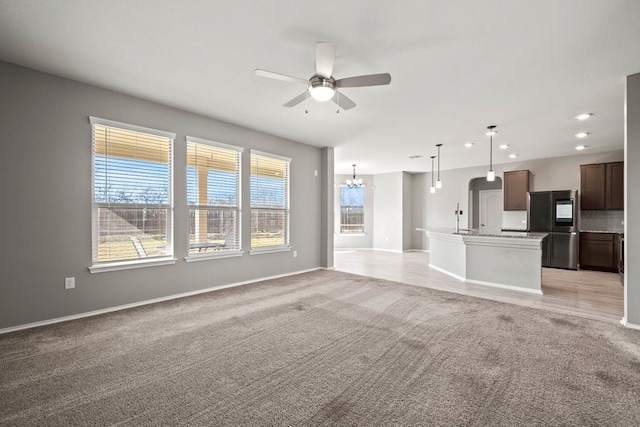 unfurnished living room with recessed lighting, light carpet, ceiling fan with notable chandelier, a sink, and baseboards