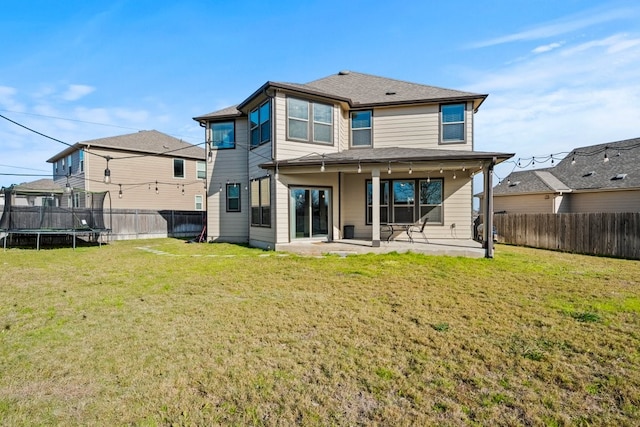 back of property with a trampoline, a patio area, a fenced backyard, and a lawn