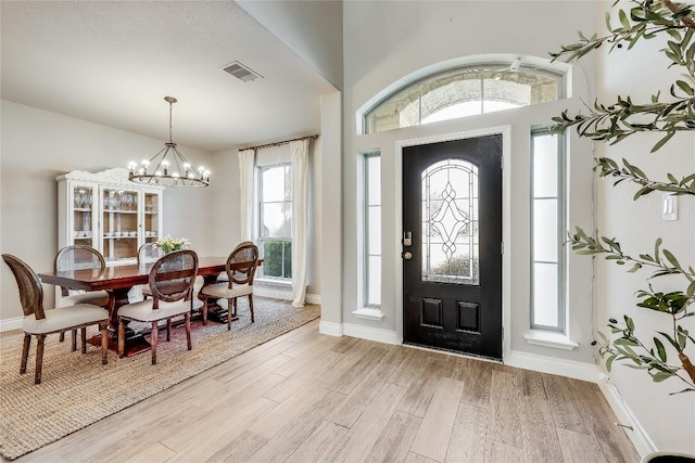 foyer featuring light wood-type flooring, baseboards, visible vents, and a notable chandelier