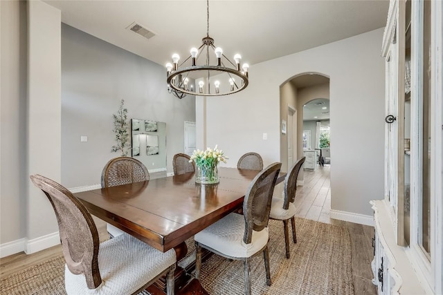 dining area with light wood-type flooring, visible vents, arched walkways, and baseboards