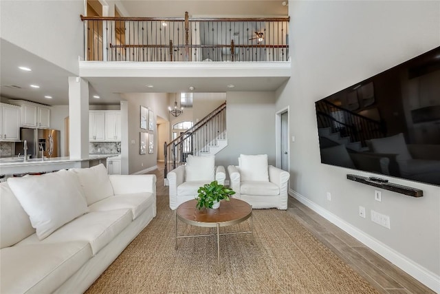 living room featuring a towering ceiling, an inviting chandelier, wood finished floors, baseboards, and stairs