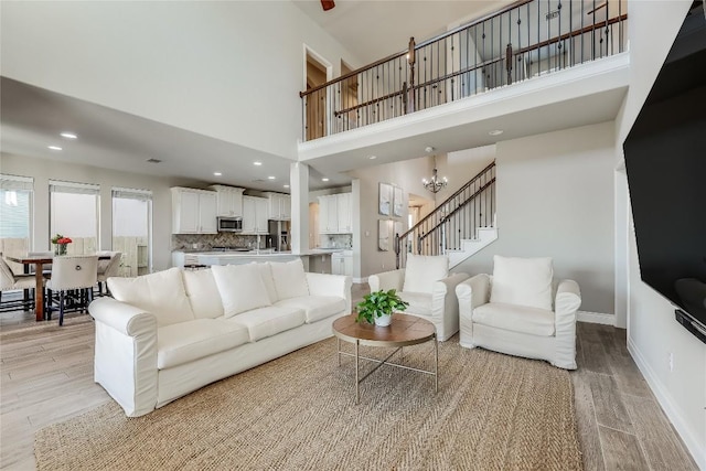 living room with a chandelier, baseboards, stairway, and light wood finished floors