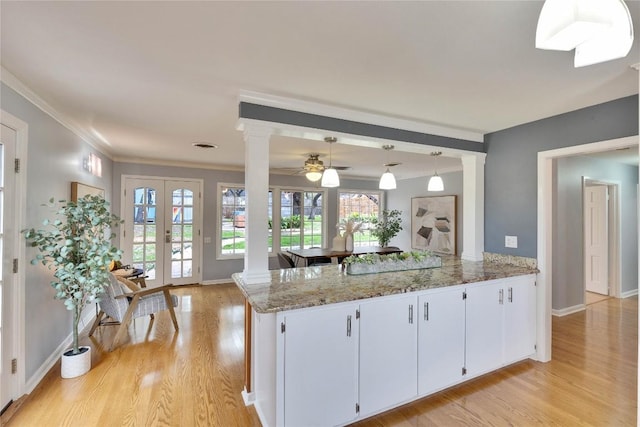 kitchen featuring light stone counters, decorative columns, hanging light fixtures, white cabinetry, and light wood-type flooring