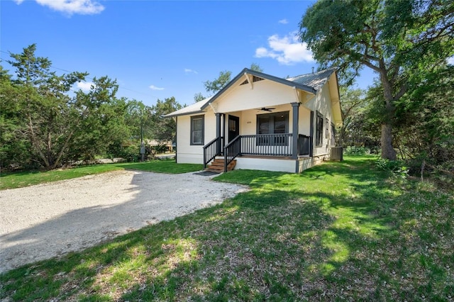 bungalow featuring covered porch, ceiling fan, a front lawn, and gravel driveway